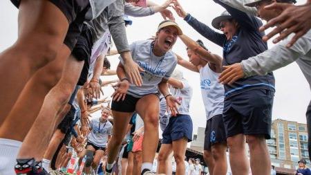 Frisbee player runs through tunnel of supporters holding hands above after victory.