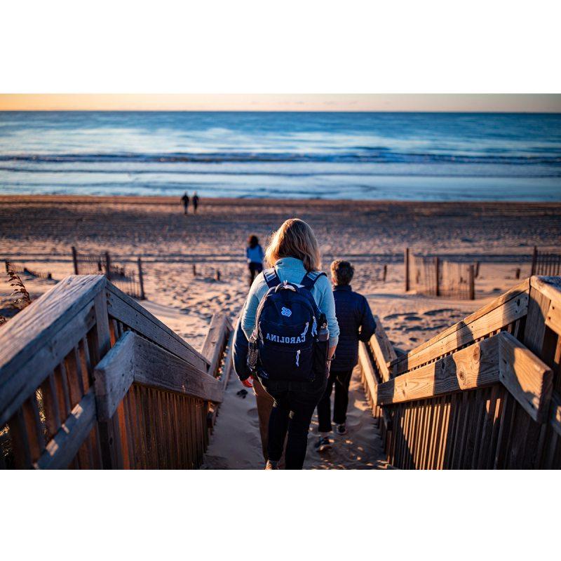 Woman with Carolina backpack walks toward the ocean at the beach