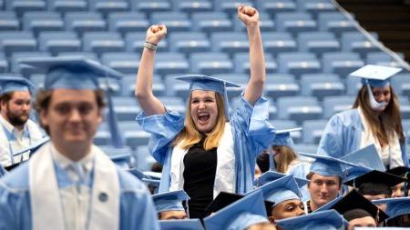 Students in commencement garb cheering and throwing hands in the air after graduating.