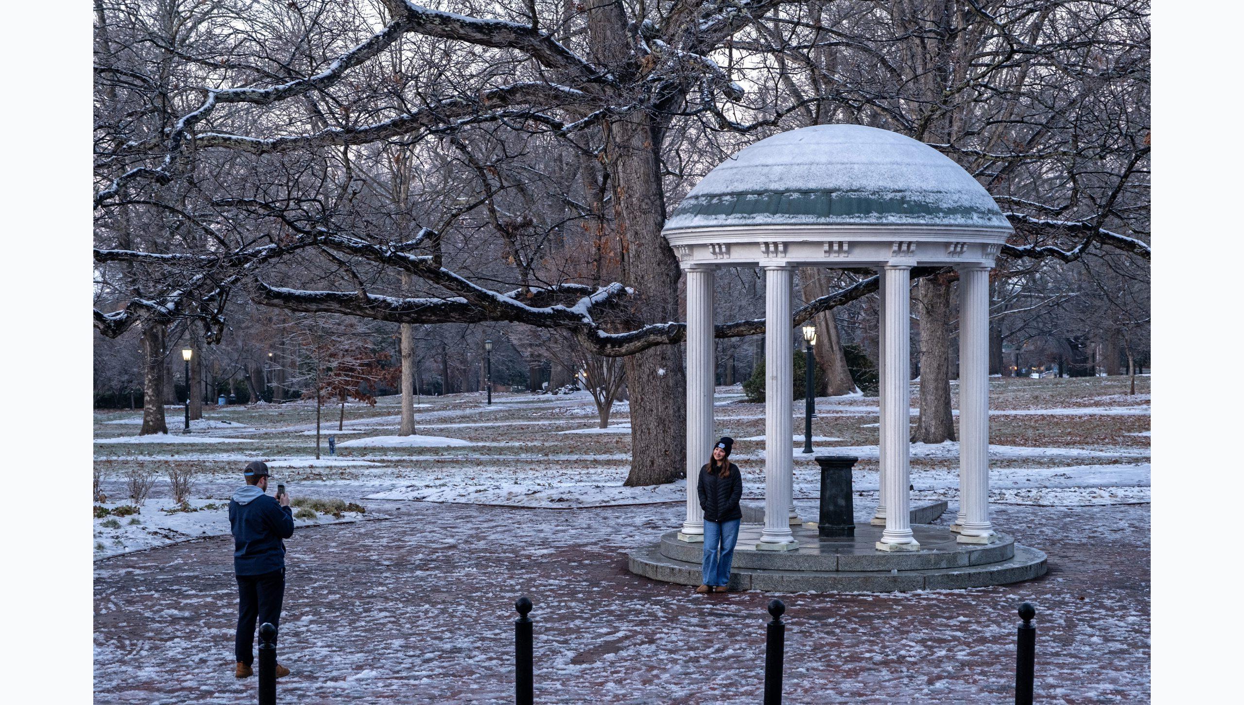 A student having her photo taken in front of the Old Well on the snow-covered campus of U.N.C Chapel Hill campus.